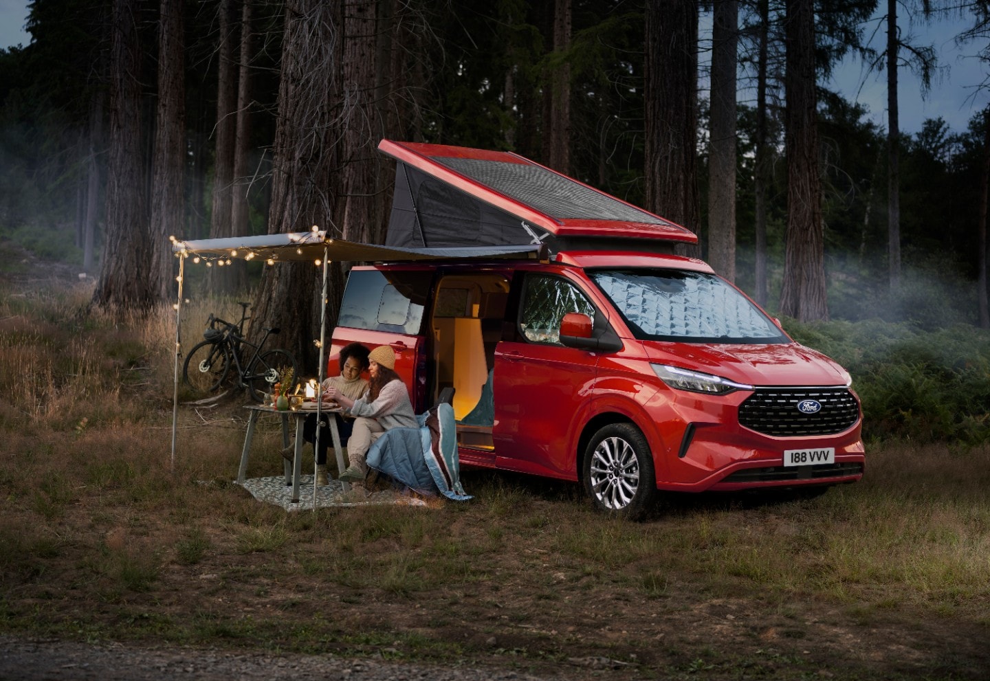 Una donna collega un caricabatterie al nuovissimo camper Ford Transit Custom Nugget Plug-In Hybrid.