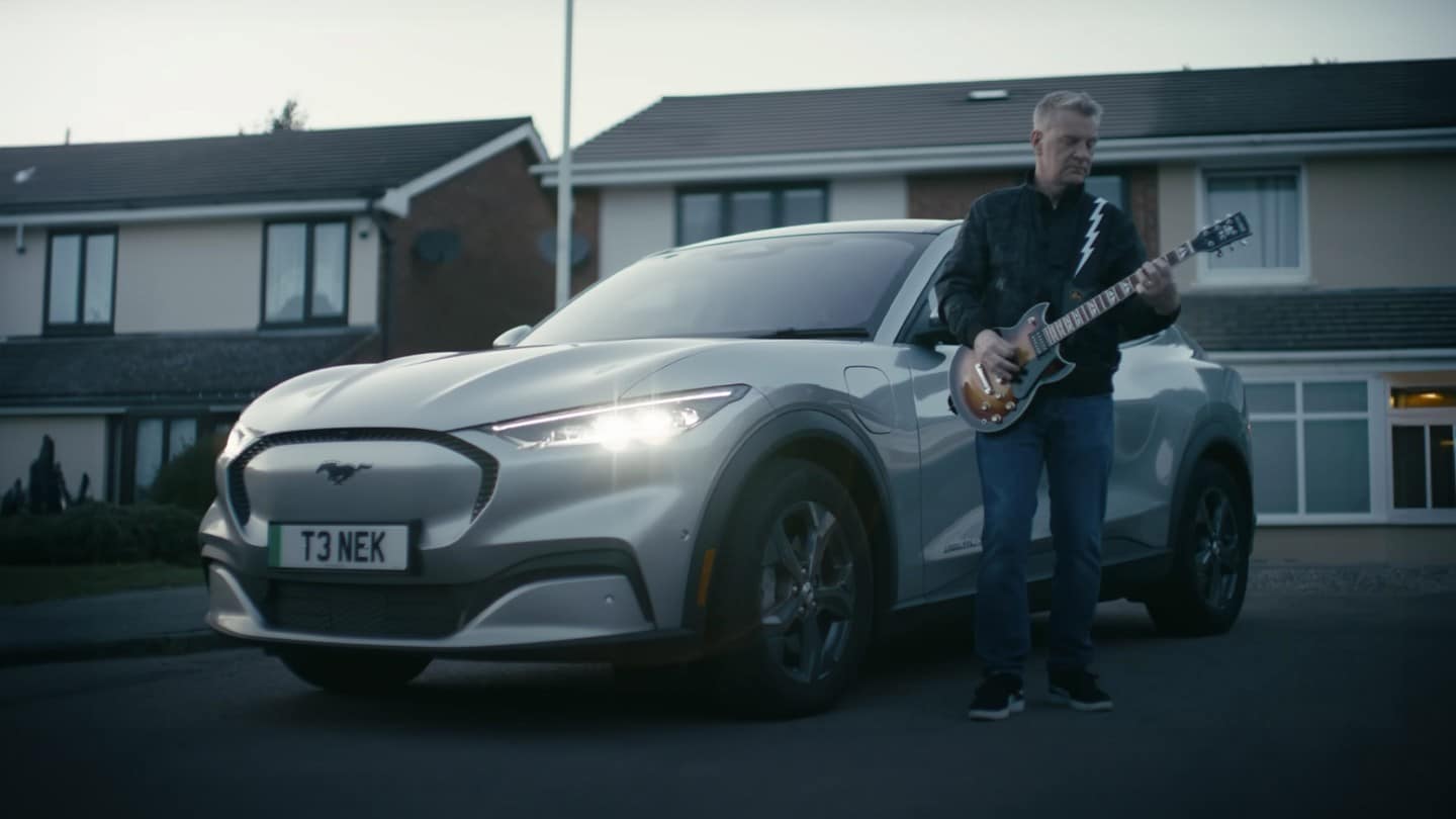 Il musicista Peter Steer è in piedi con la sua chitarra accanto alla sua Mustang Mach-E.