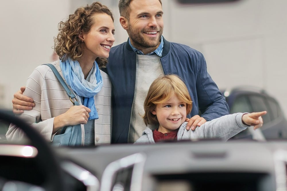 Una famiglia felice in una concessionaria, sorridente e piena di gioia.