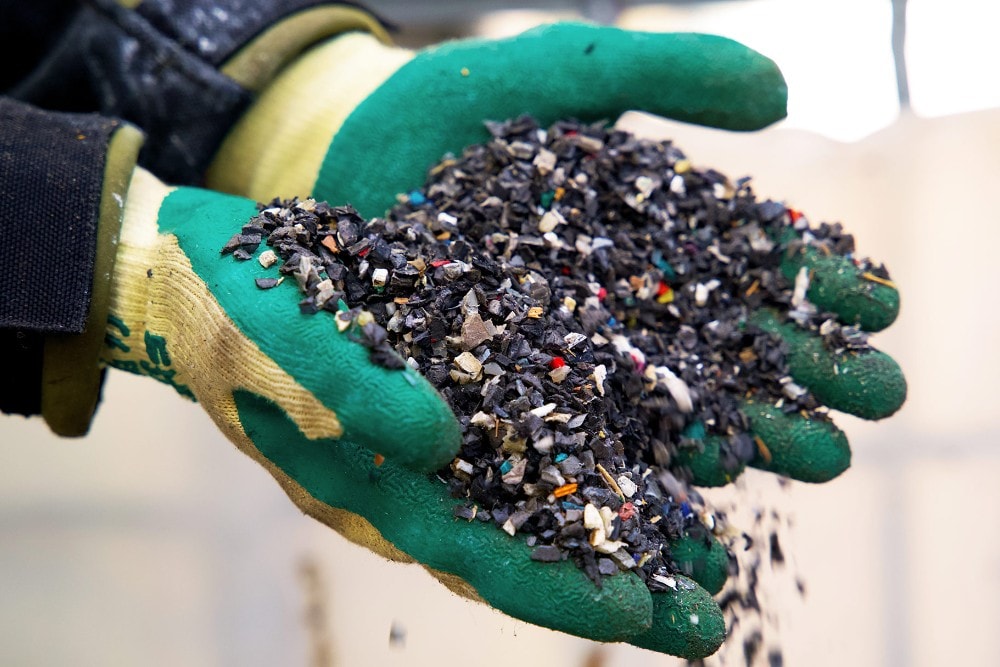 Mani con guanti di gomma che reggono pezzi di rifiuti di plastica riciclati.