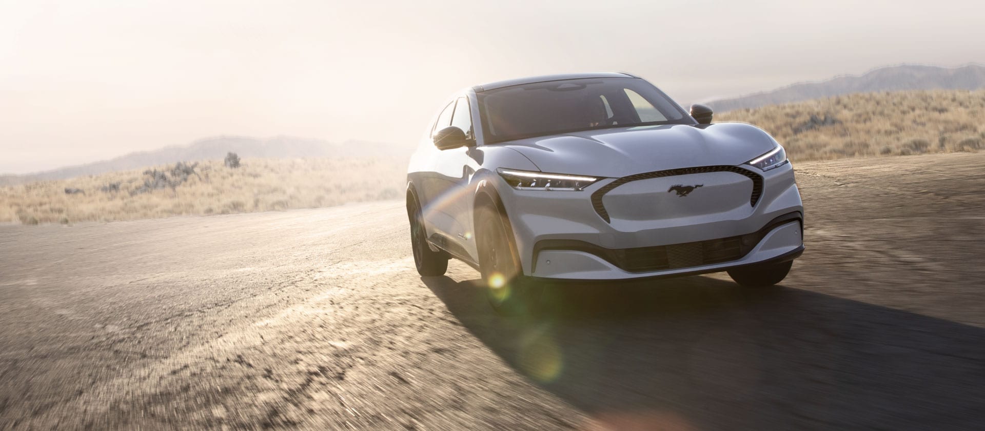Un veicolo elettrico Ford Mustang Mach-E color argento che guida su una lunga strada aperta.