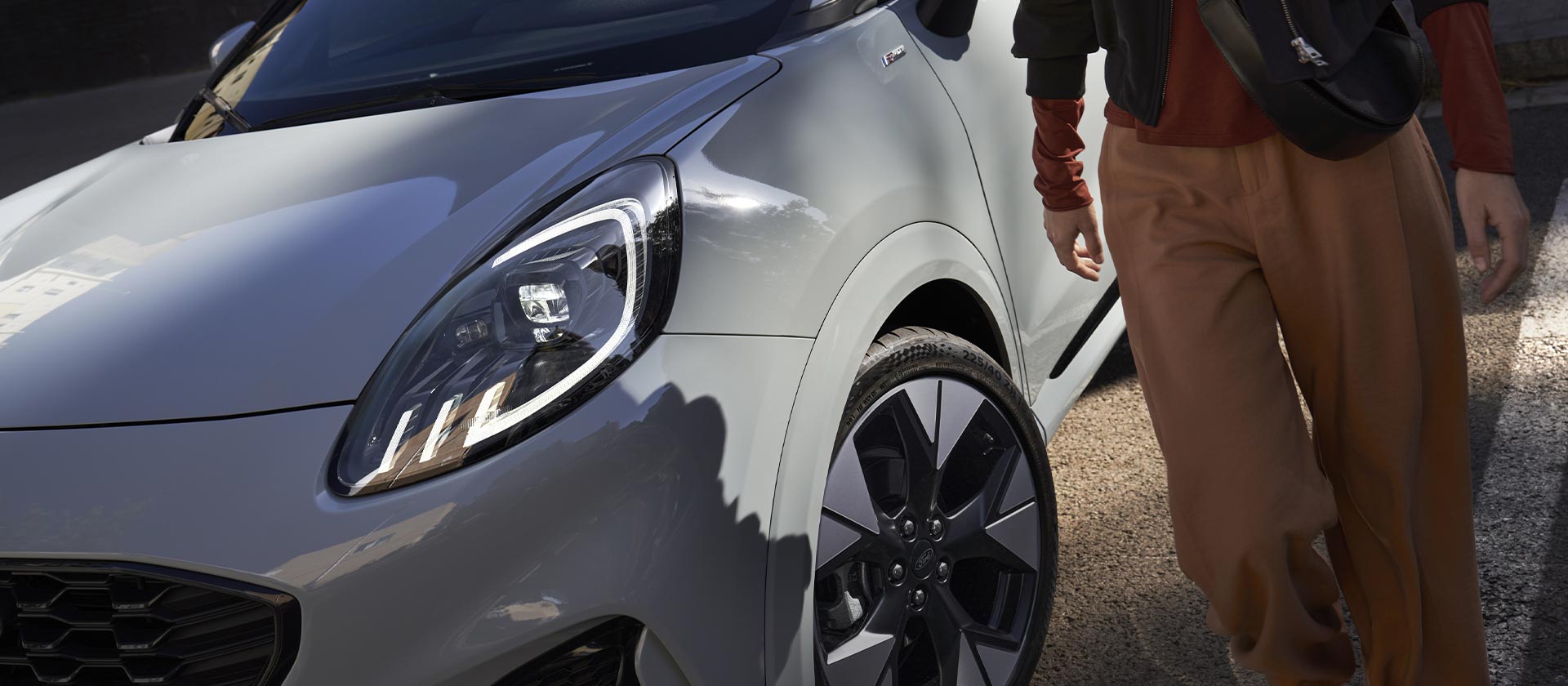 Una persona in piedi accanto a un'auto elettrica Ford Mustang Mach-E colore silver.