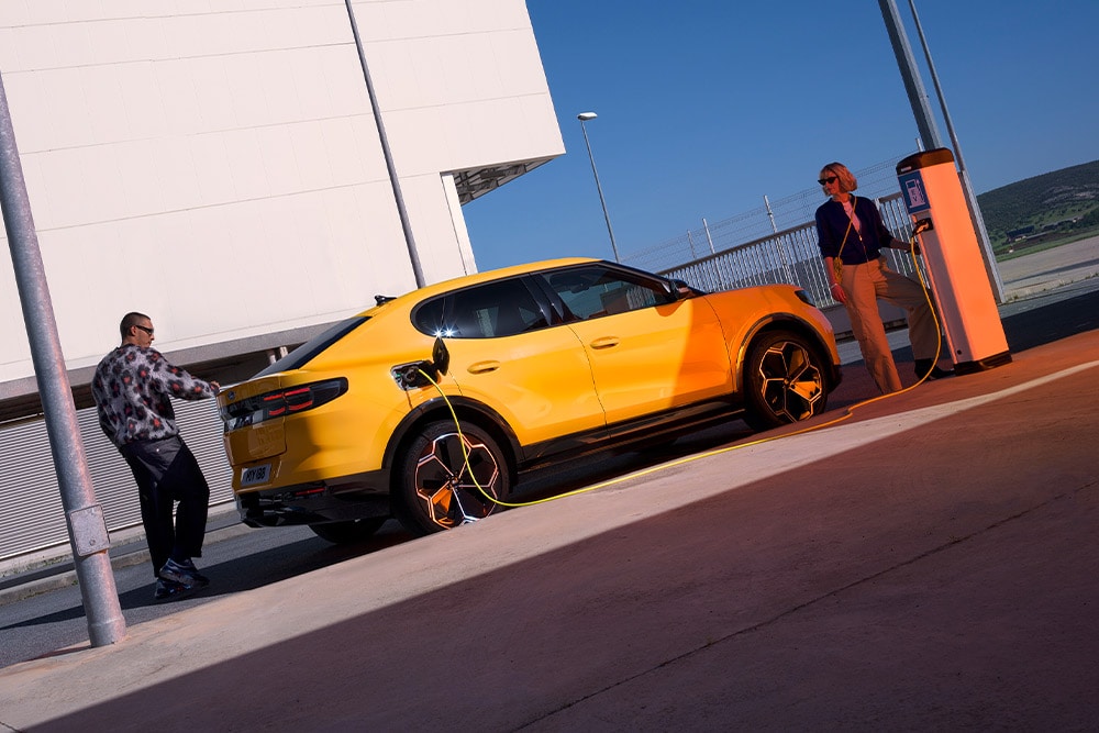 Persone che ricaricano una Ford Capri EV gialla presso una stazione di ricarica pubblica.