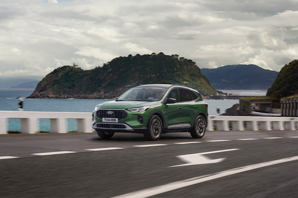 Un'auto ibrida a ricarica automatica Ford Kuga verde che percorre una strada panoramica.
