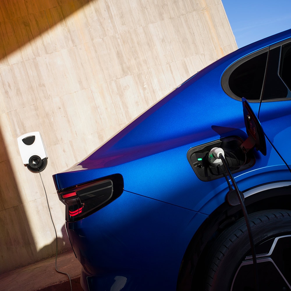 Vista posteriore di un veicolo elettrico Ford Capri blu collegato a un punto di ricarica domestica EV.
