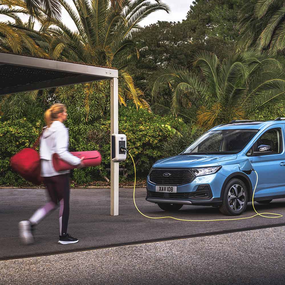 Una persona con un tappetino da yoga che cammina verso un furgone Plug-In Hybrid Ford Tourneo Connect.