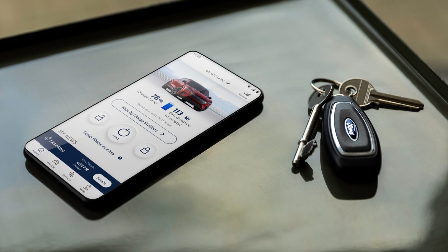 A phone showing the FordPass App on its screen sitting on a desk next to some car keys.