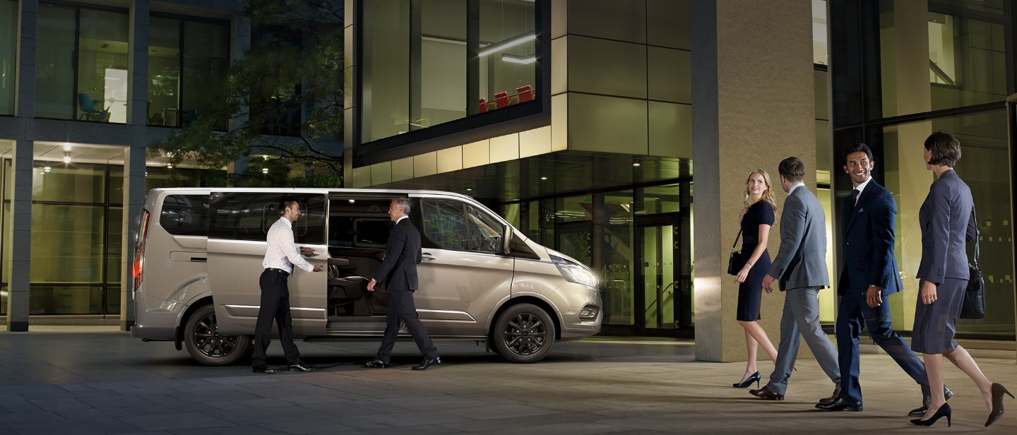 Ford Tourneo Custom in front of office building with side door open and people getting on