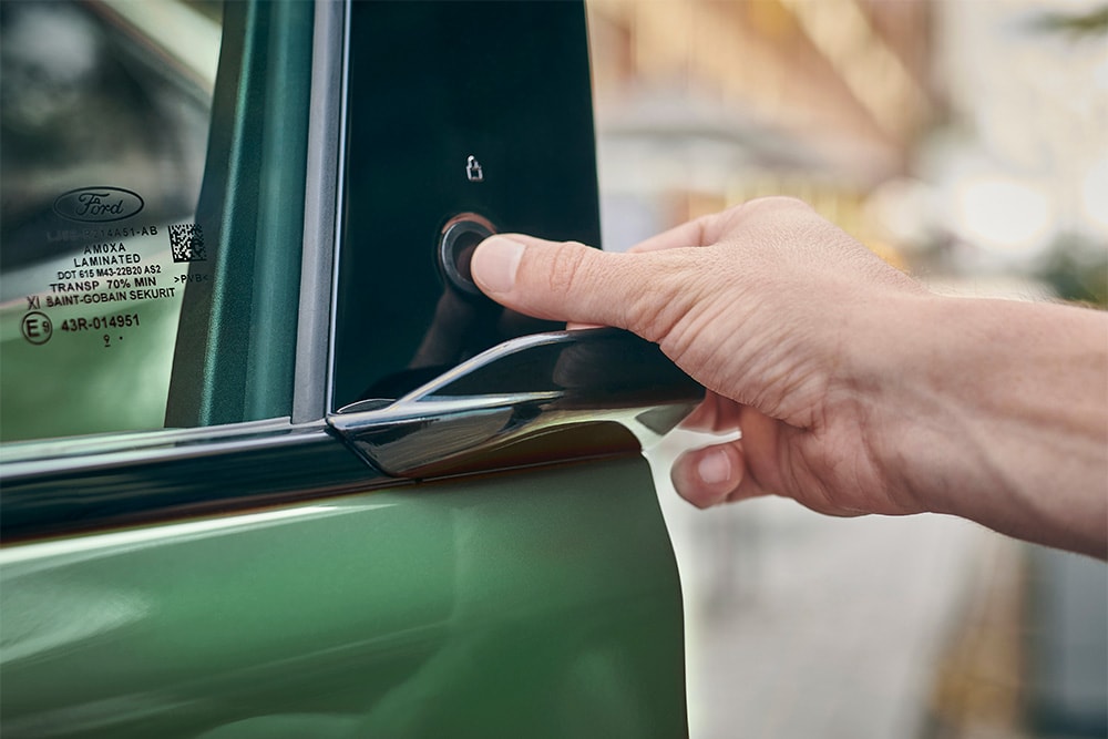Primo piano di una mano che aziona il sistema E-Latch premendo un pulsante sulla portiera di un Ford Mustang Mach-E verde.
