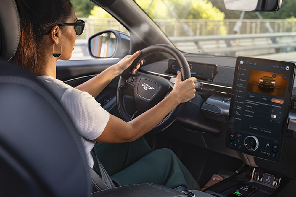 Una donna guida la Mustang Mach-E con le mani sul volante, mentre il touchscreen da 15,5 pollici mostra i dettagli dell'auto