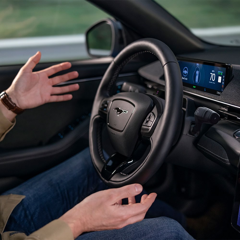 Un paio di mani fluttuano vicino al volante della Mustang Mach-E, dimostrando la tecnologia di guida autonoma BlueCruise