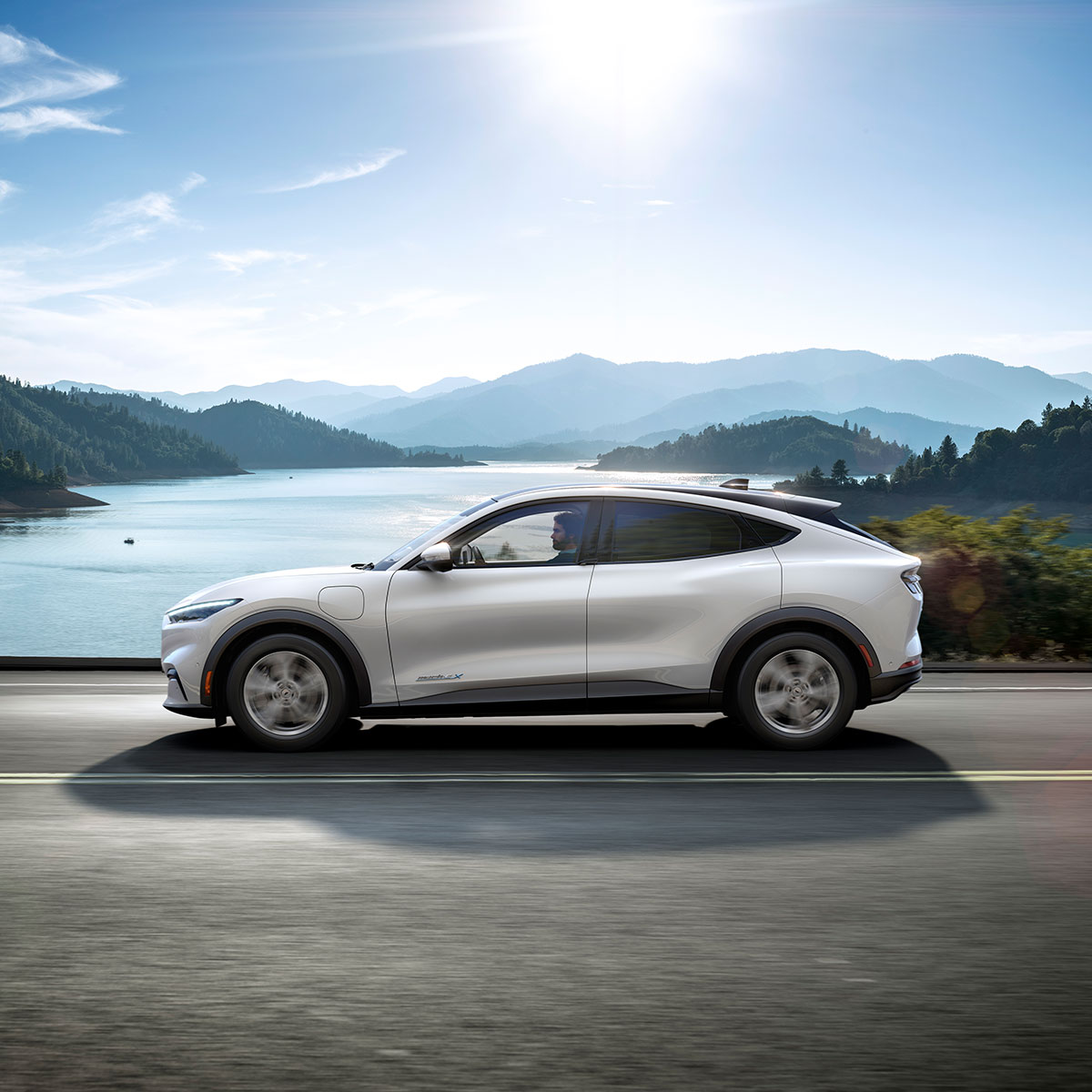 Ford Mustang Mach-E All Electric grigia in movimento che costeggia scogliere soleggiate e mare