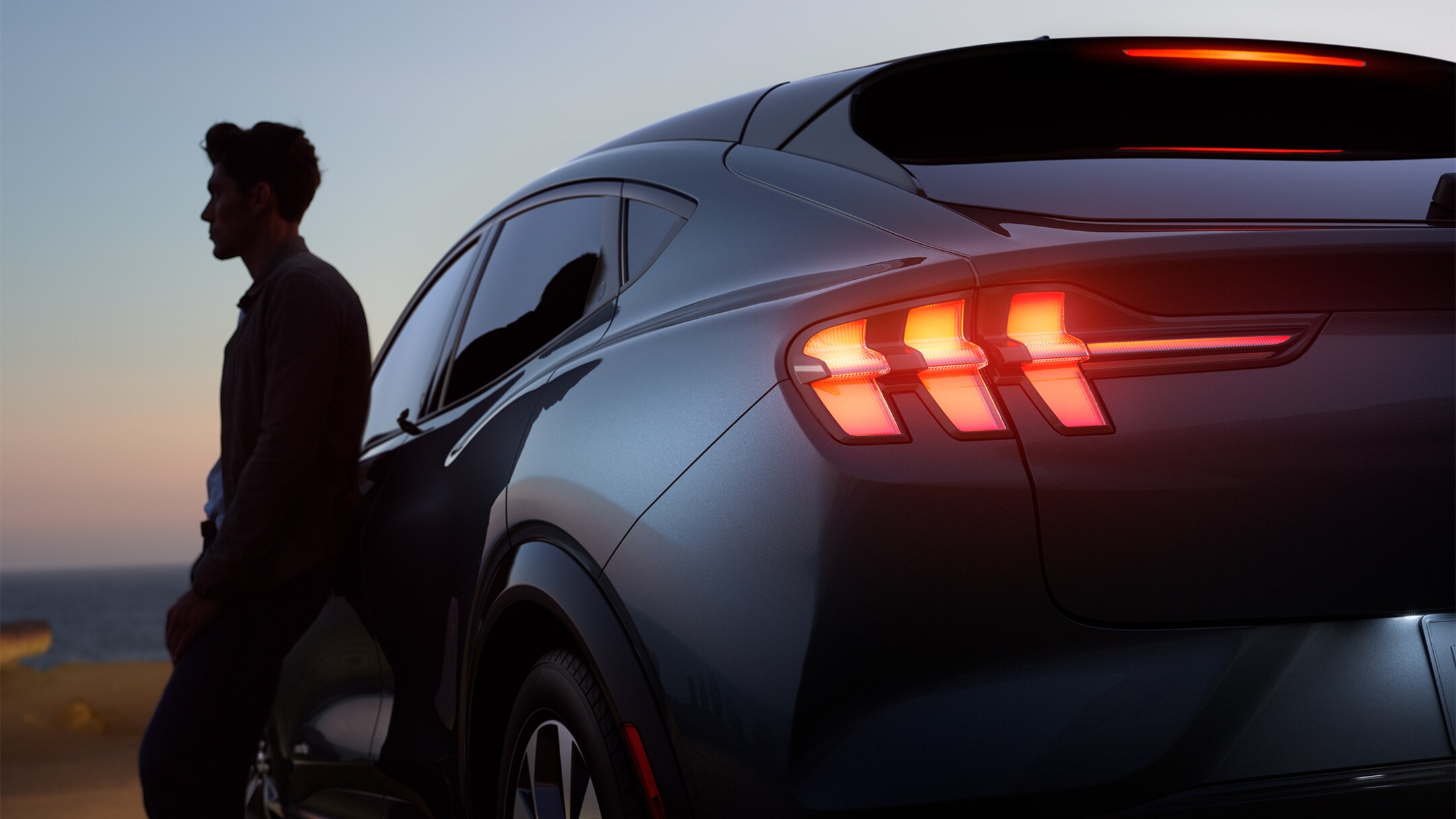 Un uomo appoggiato a una Ford Mustang Mach-E al tramonto