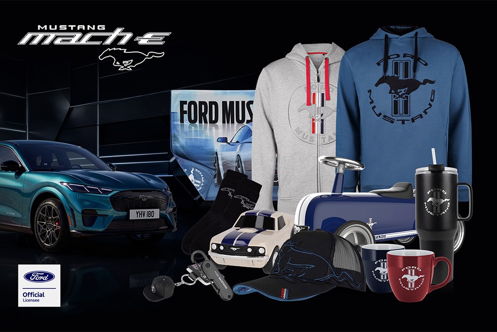 Collezione di articoli a marchio Ford con vari modelli Ford sullo sfondo, tra cui ombrelli, tazze e capi di abbigliamento con il logo Ford.