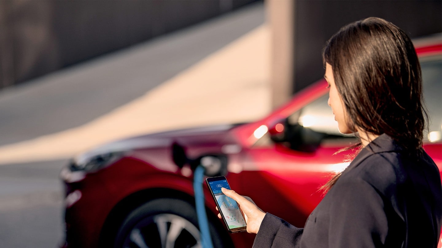 Donna che controlla il suo telefono durante la ricarica della Ford Kuga