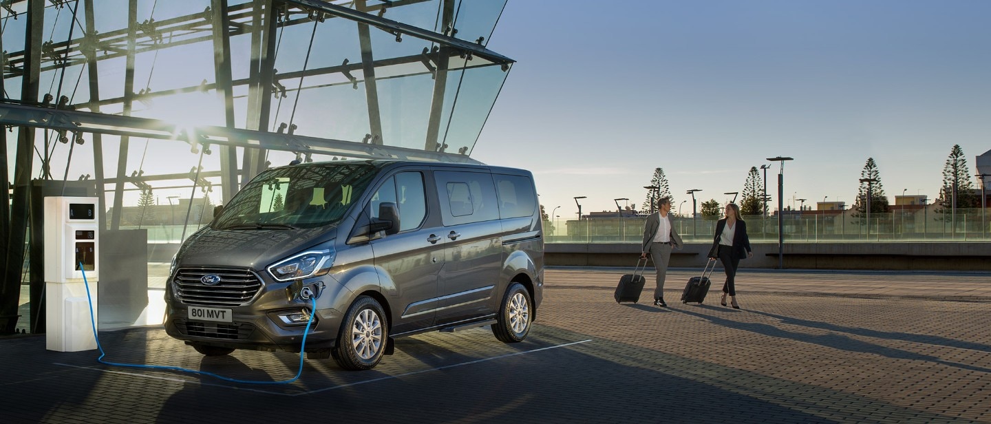 Ford Tourneo Custom PHEV being charged next to modern building