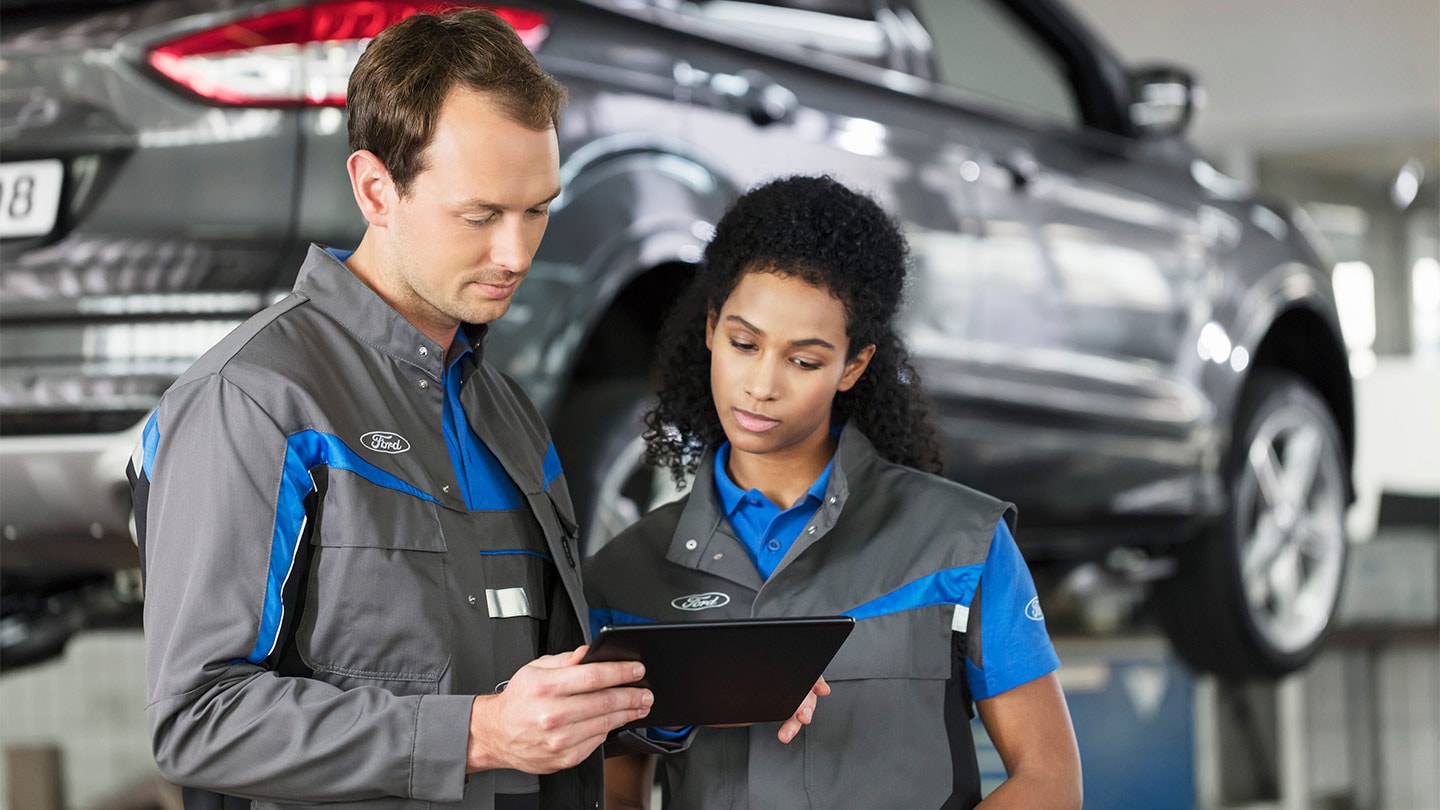 Due specialisti delle riparazioni Ford controllano il loro sistema di prenotazione dei servizi online su un telefono
