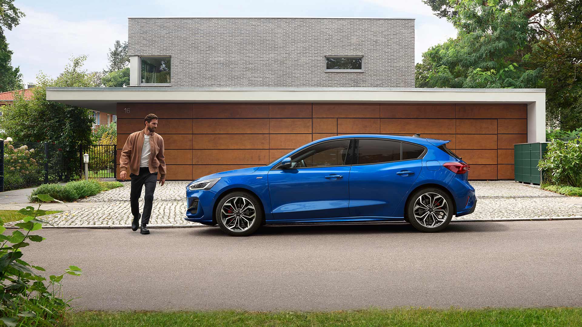 Un uomo che si avvicina a una Ford Focus blu parcheggiata fuori da una casa.