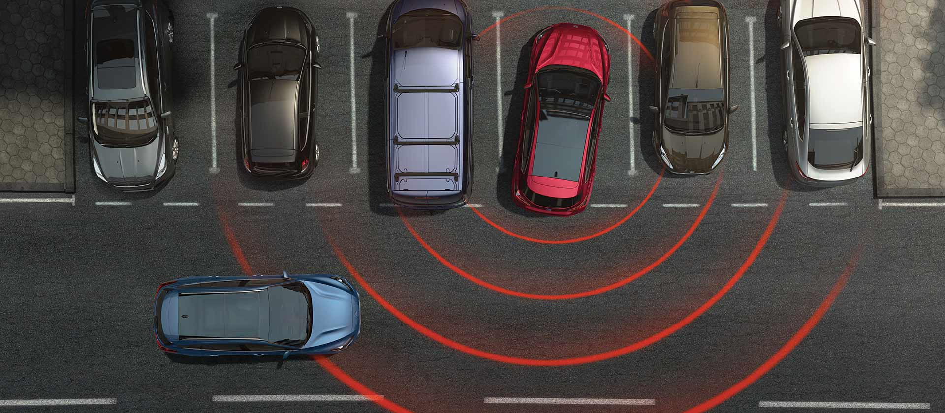 Visuale dall'alto di una fila di auto parcheggiate. Una Ford Focus rossa esce in retromarcia sfruttando i sistemi di assistenza alla guida avanzati, rappresentati con un radar di linee rosse che evidenziano i pericoli nelle vicinanze.