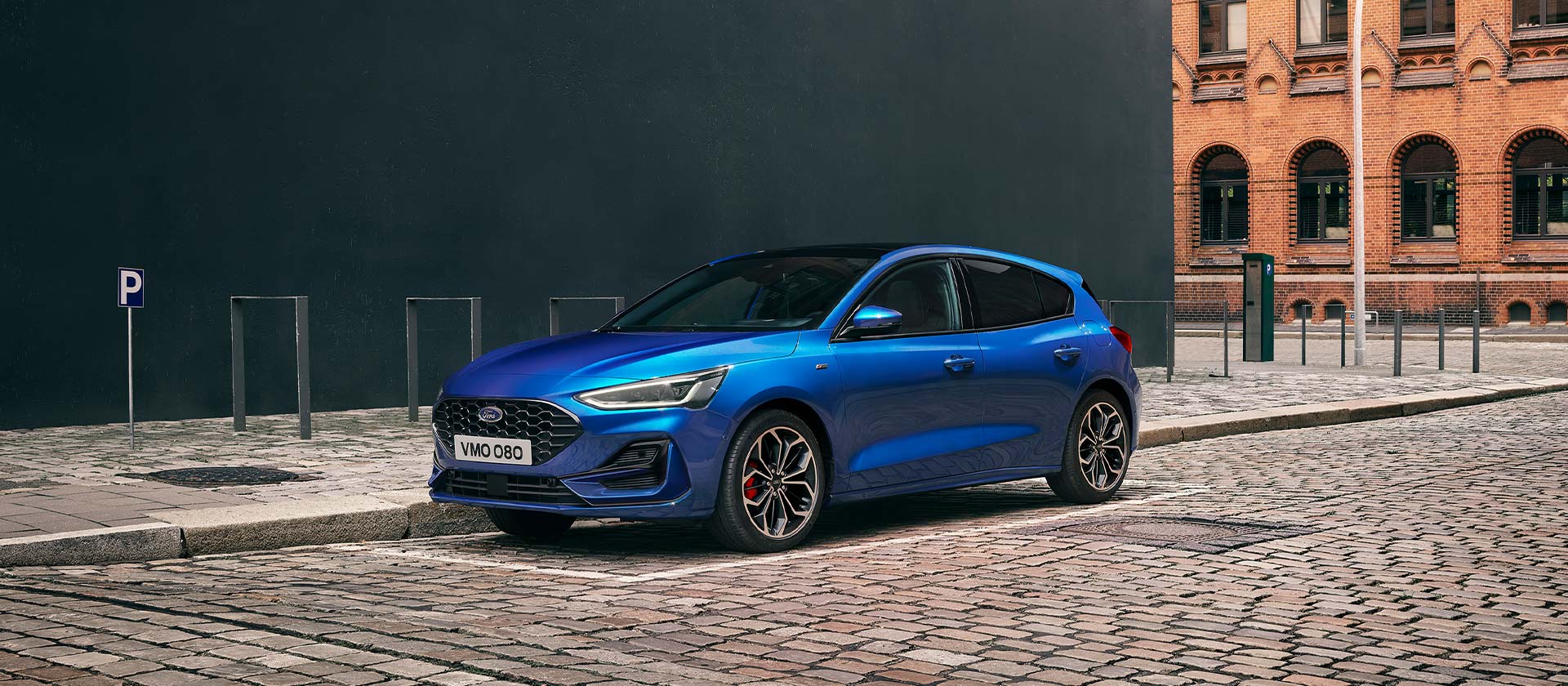 Una Ford Focus berlina blu parcheggiata su una strada di ciottoli in un contesto urbano.