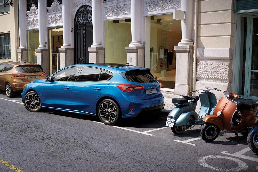 Una Ford Focus blu che parcheggia in città utilizzando la funzione Active Park Assist.