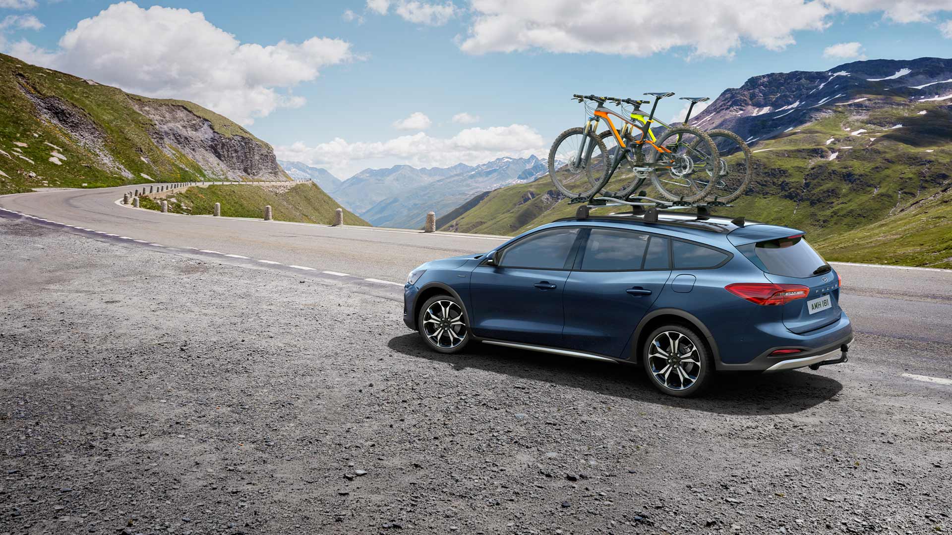Una Ford Focus blu con biciclette sul tettuccio che percorre una strada panoramica di montagna.