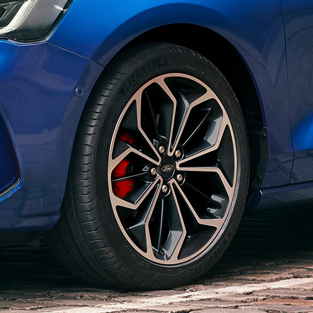 Primo piano dei cerchi in lega grigi con pinze dei freni rosse su una Ford Focus blu.