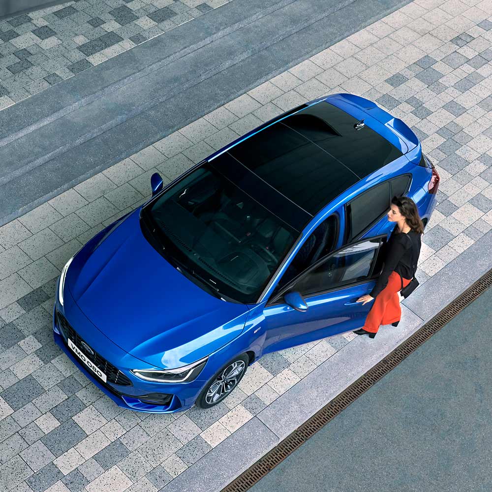 Visuale dall'alto di una donna che sale sulla sua Ford Focus blu con tetto panoramico in vetro.