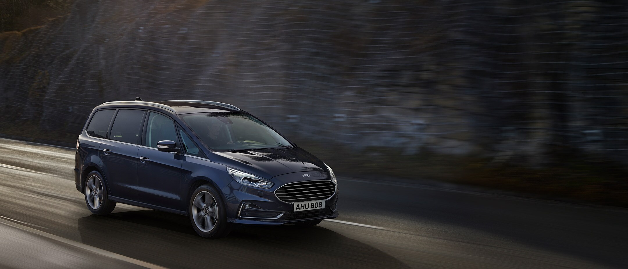 Blue metallic Ford Galaxy driving on mountain road Blue metallic Ford Galaxy driving on mountain road