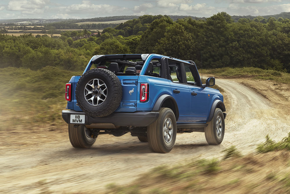 Vista posteriore di un Ford Bronco blu che attraversa un paesaggio rurale.