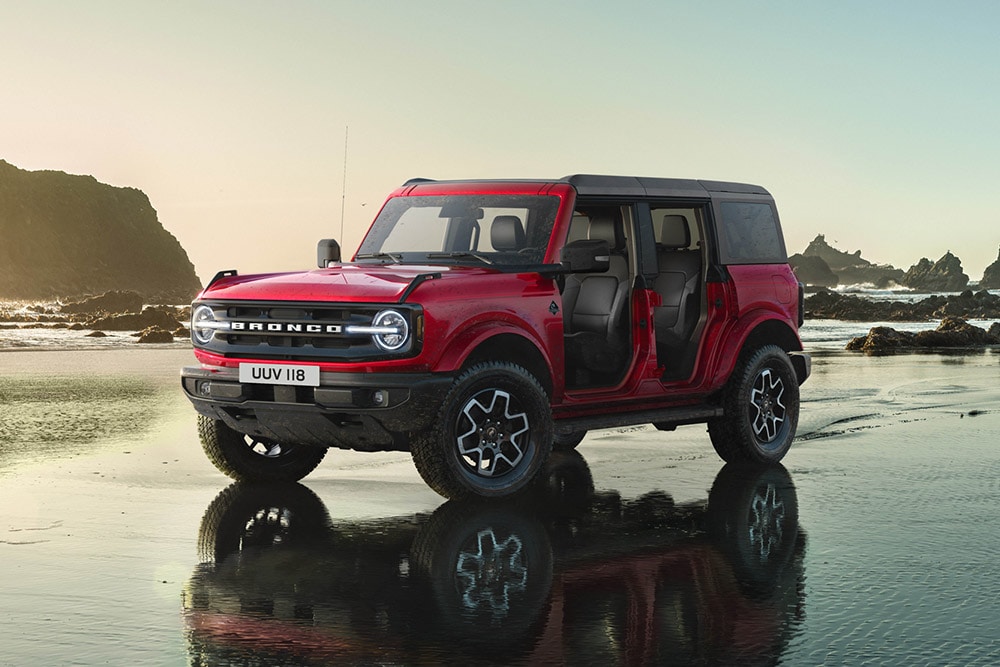 Vista laterale di un Ford Bronco rosso senza portiere parcheggiato su una spiaggia bagnata.