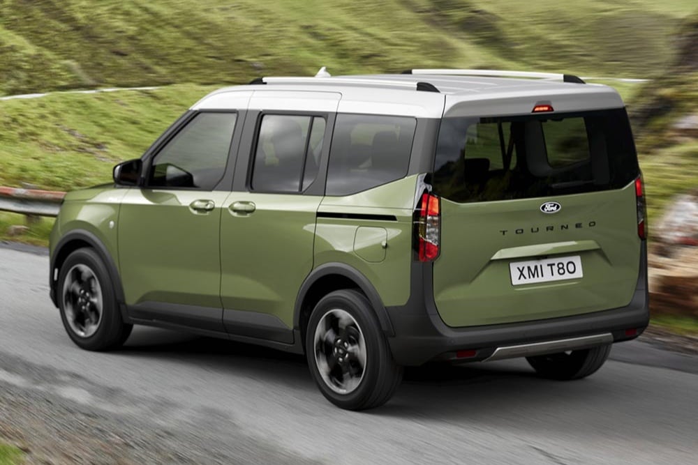 Un Ford Tourneo Courier verde guida su una strada tortuosa con colline verdi sullo sfondo.