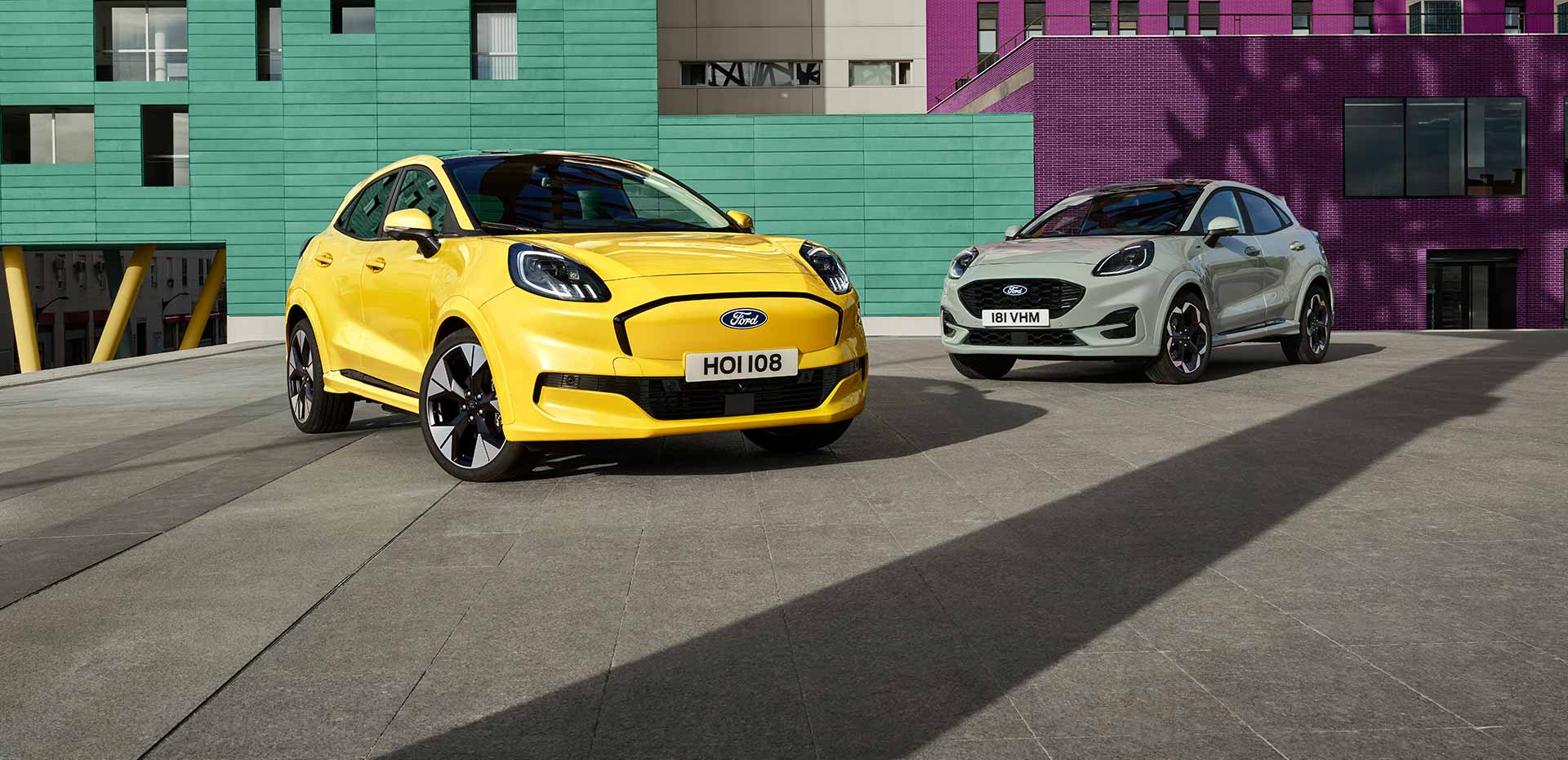 Uno giallo Ford Puma-e e uno grigio Ford Puma, parcheggiati di fronte a un edificio.