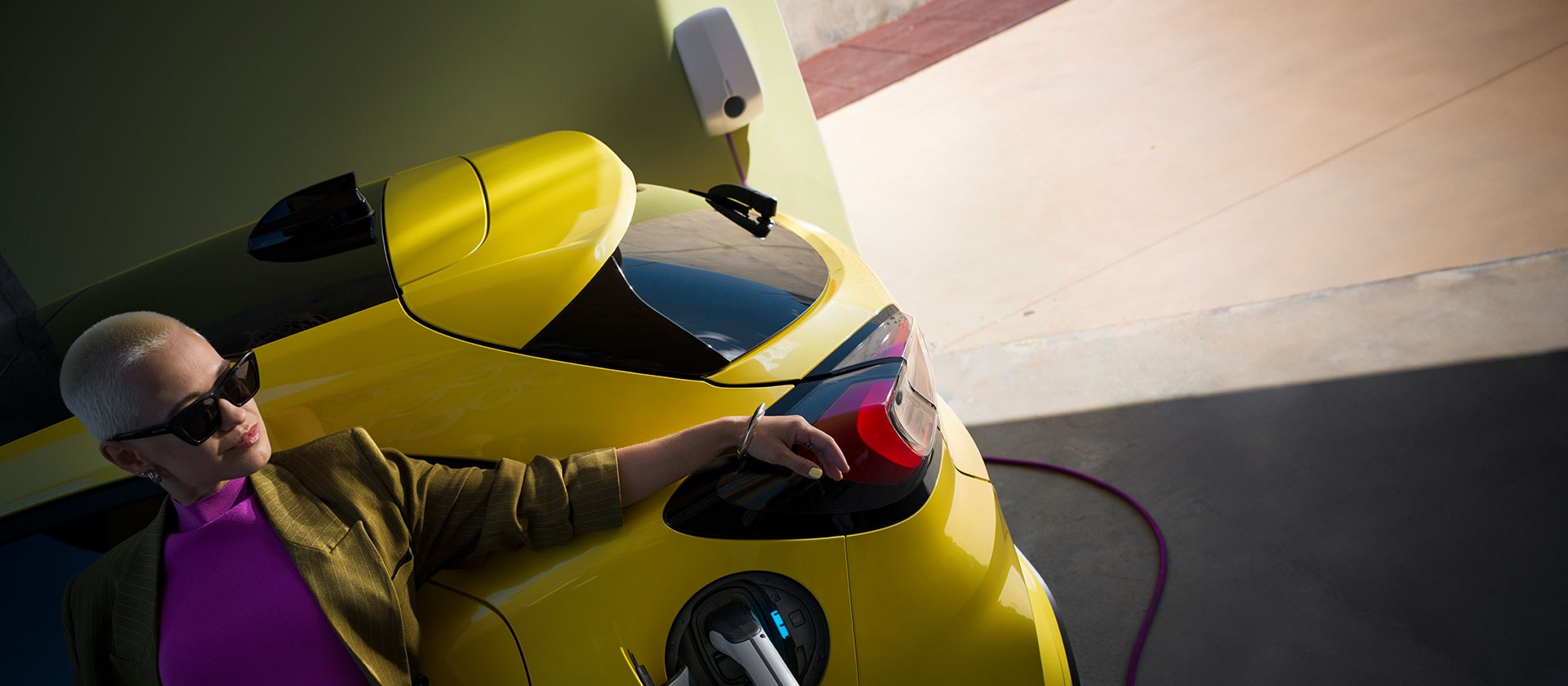Un primo piano della parte posteriore di un Ford Puma Gen-E® elettrico giallo, collegato a una wallbox domestica.