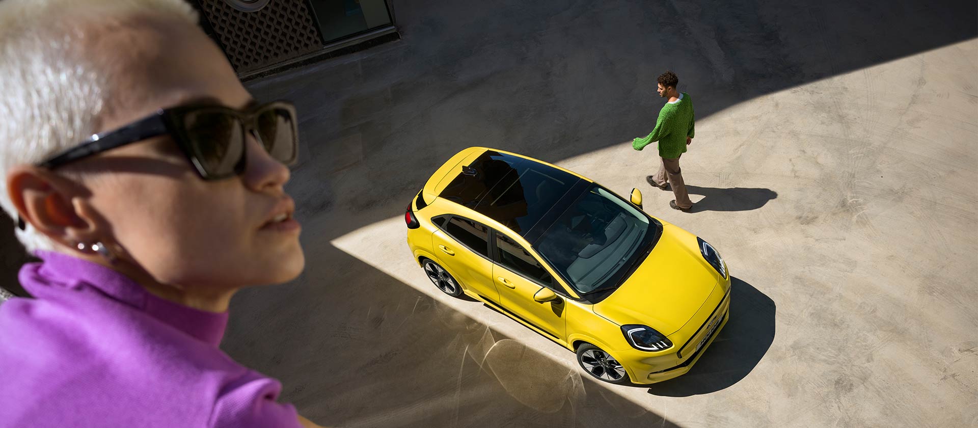 Vista a volo d'uccello di un Ford Puma Gen-E® elettrico giallo. Persona in viola in primo piano.