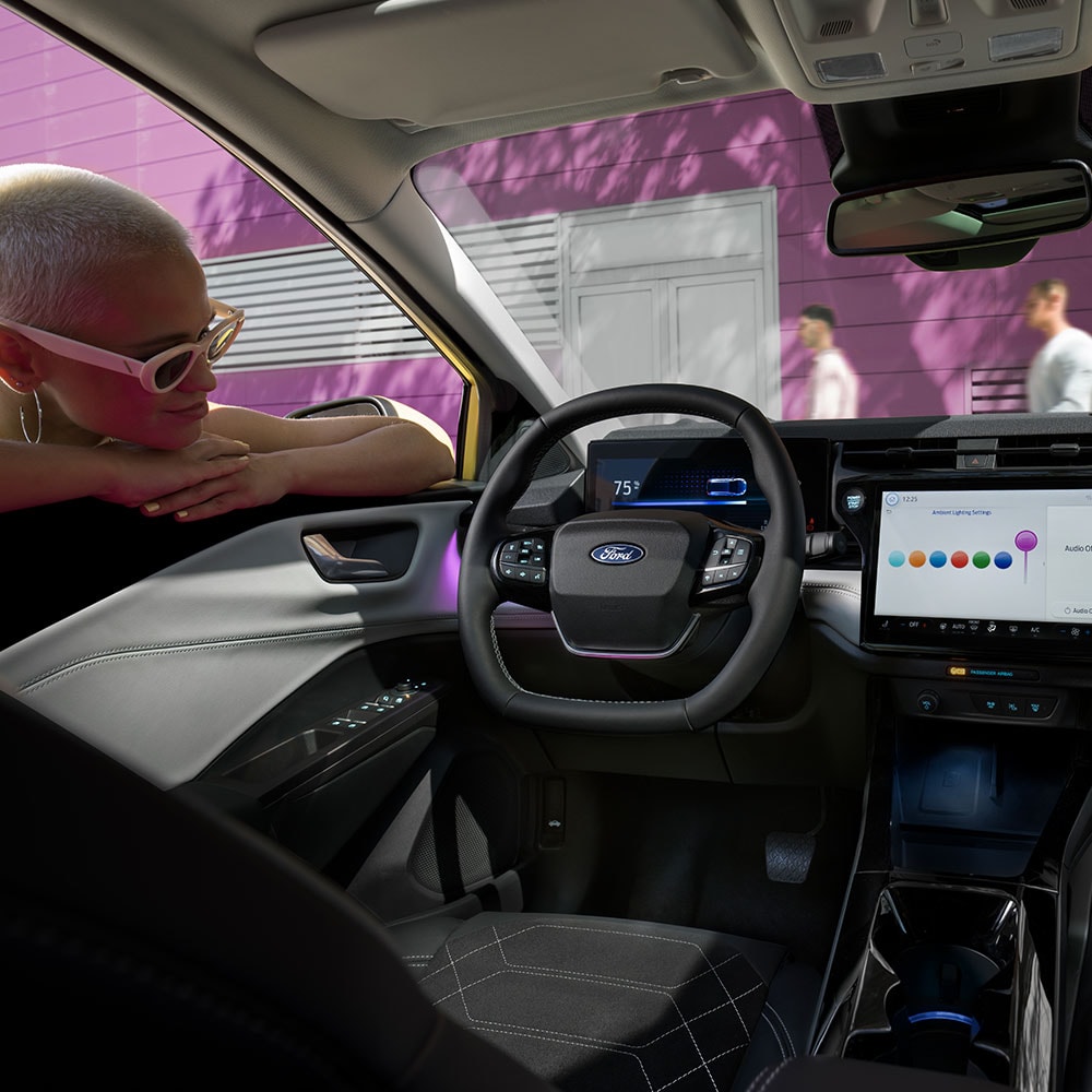 Interni del Ford Puma Gen-E® elettrico, con una persona che guarda l'ampio schermo dell'infotainment attraverso il finestrino.