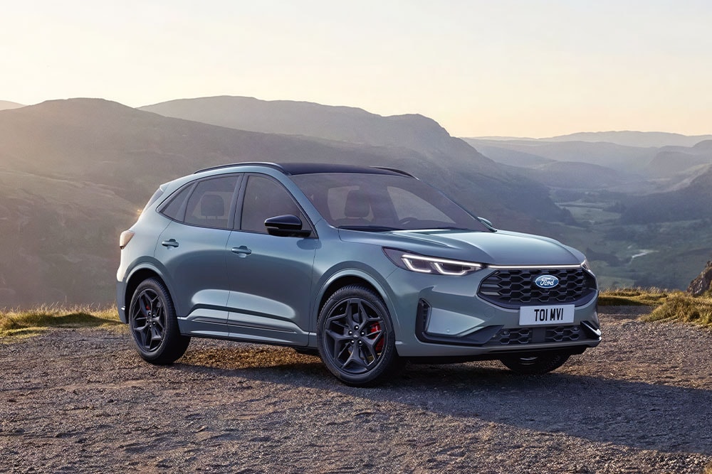 Una Ford Kuga grigia parcheggiata su una strada sterrata di montagna al tramonto.