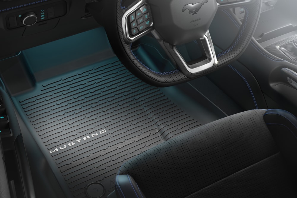 Vista interna di una Ford Mustang che mostra il volante e un tappetino antiscivolo con il marchio 'MUSTANG'.