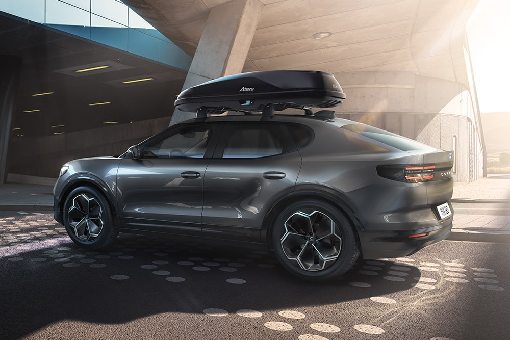 Side 3/4 view of a dark Ford Capri with a roof box, parked under a modern building structure.