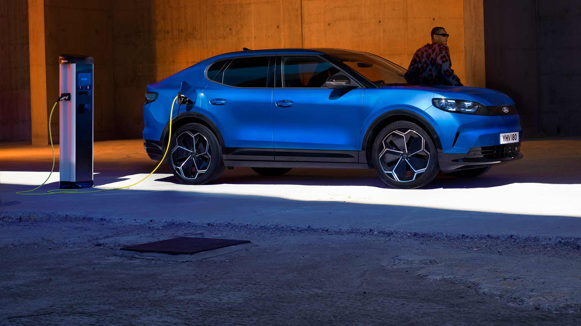 Un Ford Capri® elettrico blu collegato a una stazione di ricarica pubblica per veicoli elettrici.