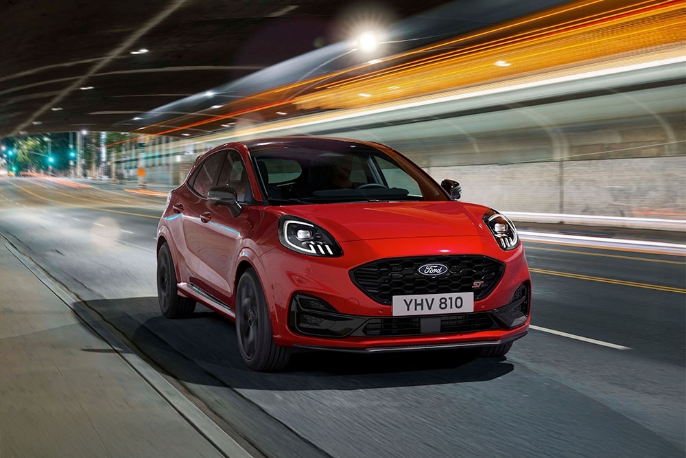 Un SUV sportivo Ford Puma ST rosso percorre una strada cittadina illuminata di notte.