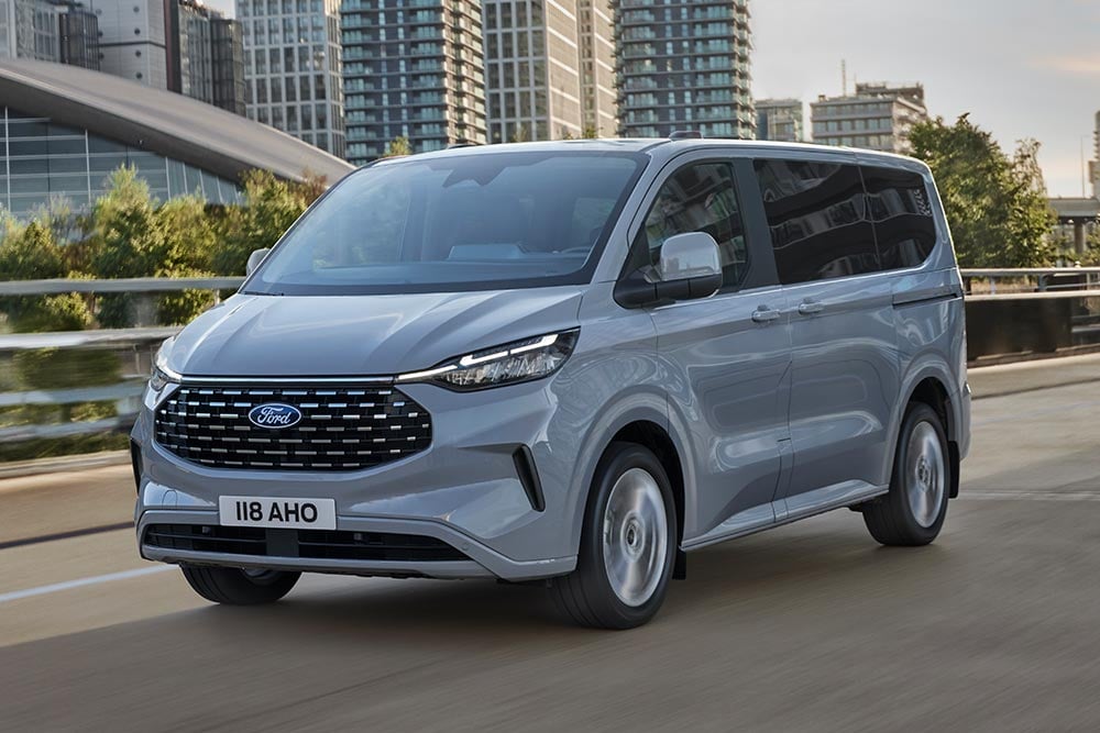 Un Ford Tourneo Custom argentato percorre una strada cittadina.
