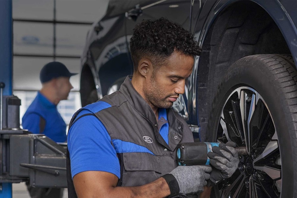 Un tecnico Ford usa un utensile elettrico per lavorare su una ruota dell'auto. Un altro tecnico è sullo sfondo. 