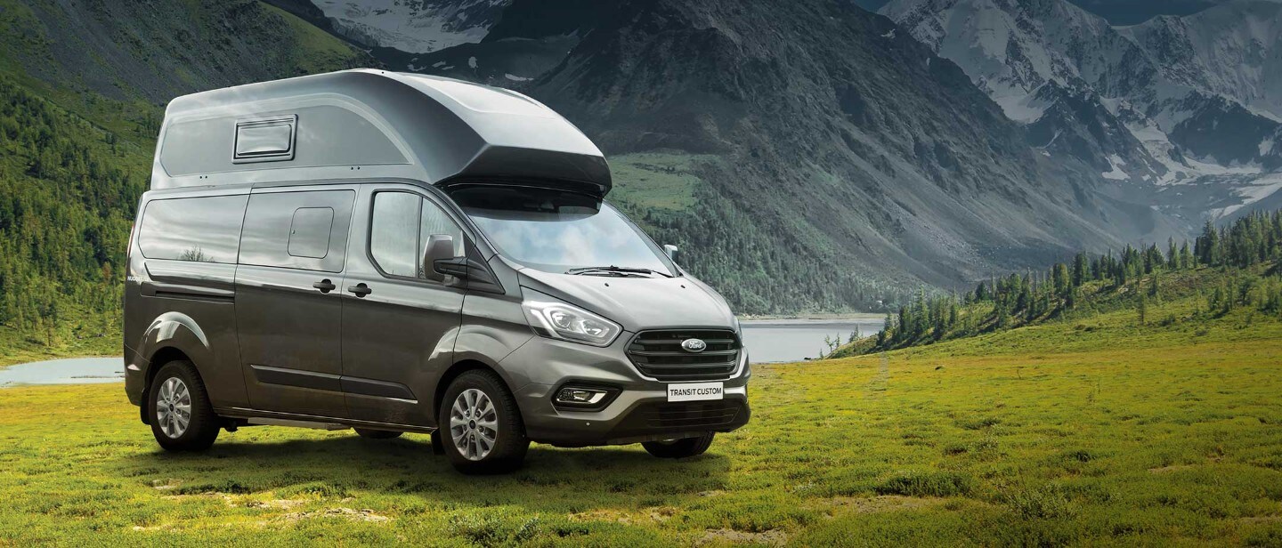 Transit Custom Nugget Plus parcheggiato sull'erba vicino alle montagne Transit Custom Nugget Plus parcheggiato sull'erba vicino alle montagne