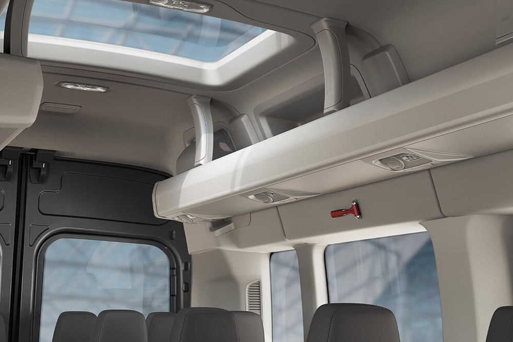 Interior of a Ford Transit Minibus, showing a sunroof, overhead storage, and an emergency hammer above passenger seats.