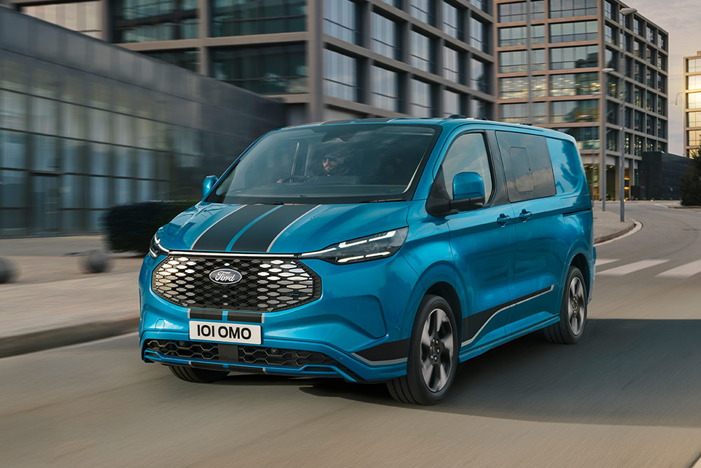 Un furgone a doppia cabina Ford E-Transit Custom Sport blu percorre una strada cittadina.
