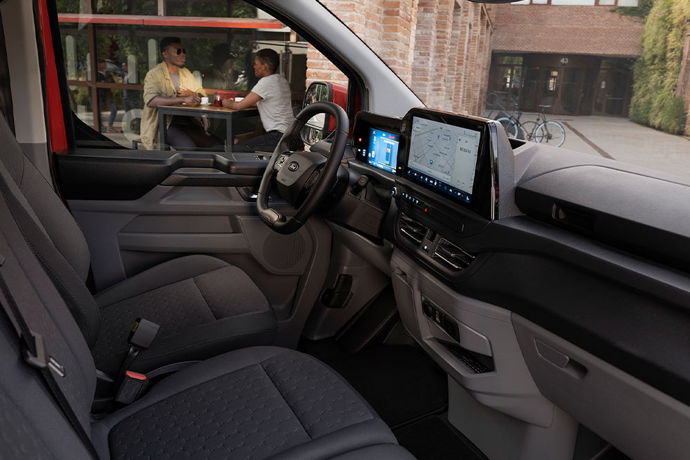 Una persona seduta al posto di guida di un furgone elettrico E-Ford Transit Custom rosso.