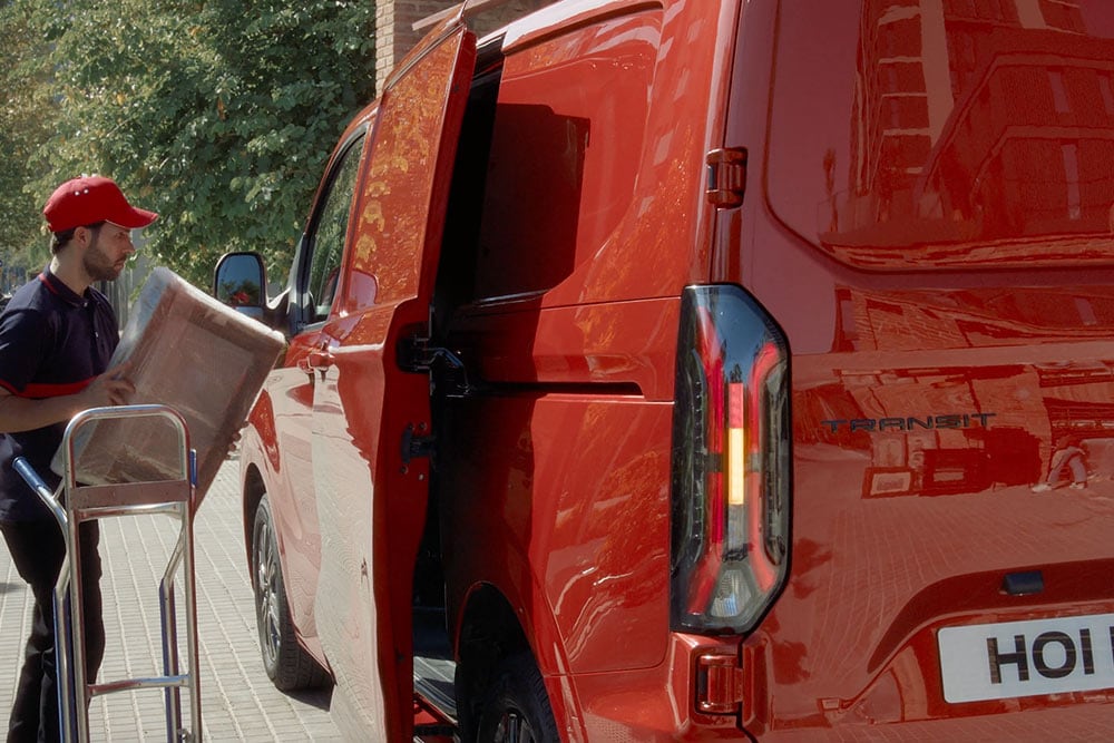 Un corriere scarica i pacchi da un Ford Transit Custom rosso.