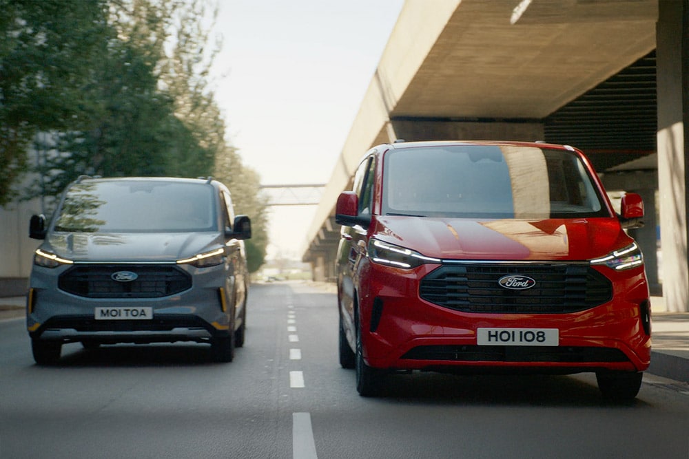 Un furgone Ford Transit Custom grigio e rosso percorre un tratto autostradale.