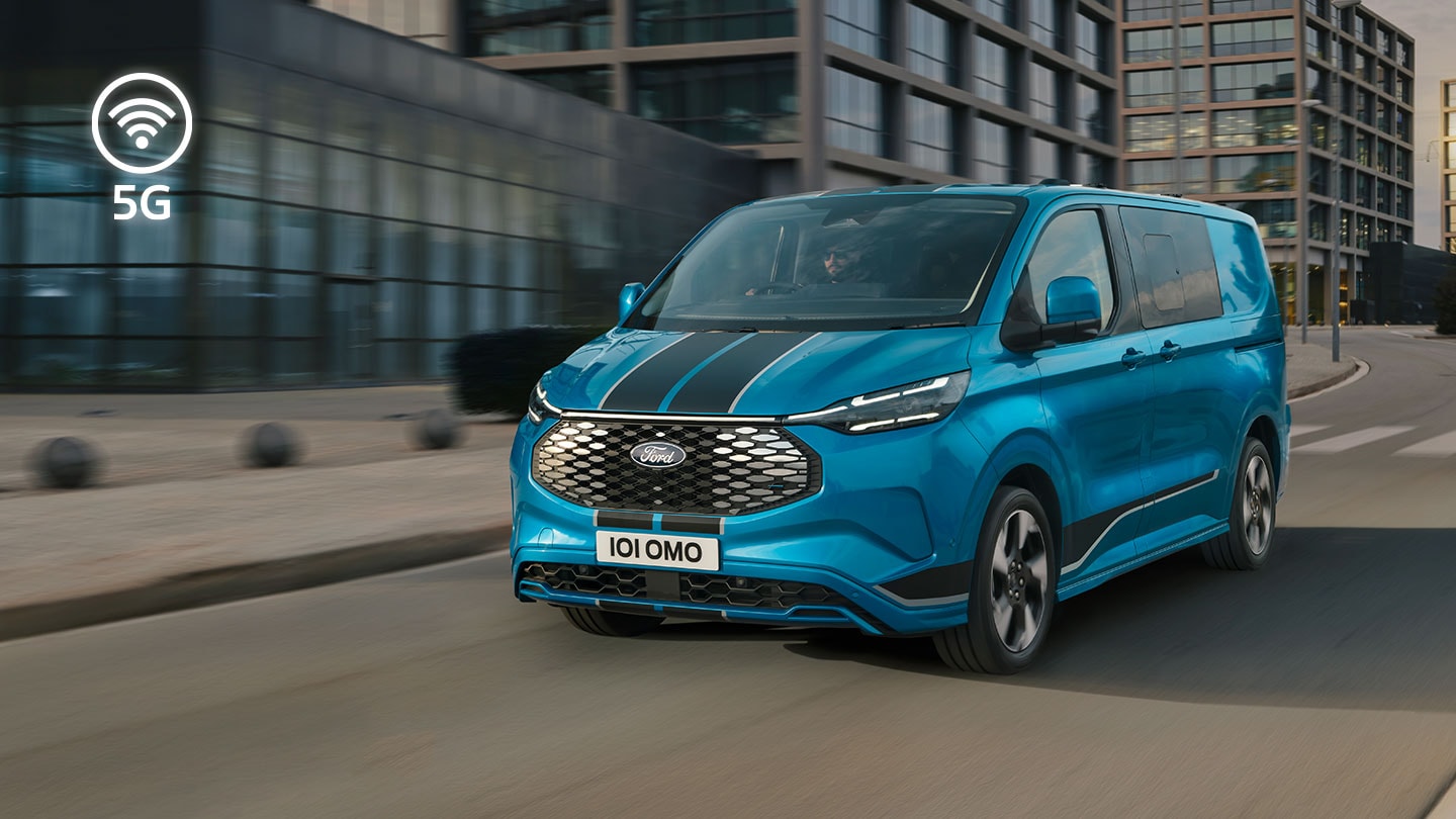 Un furgone elettrico Ford E-Transit Custom blu percorre una strada cittadina.